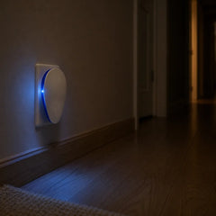 Plug-in pest repeller glowing as a soft blue night light in a dark hallway
